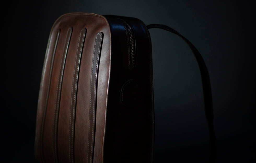 brown leather backpack with on strap showing, dark background.