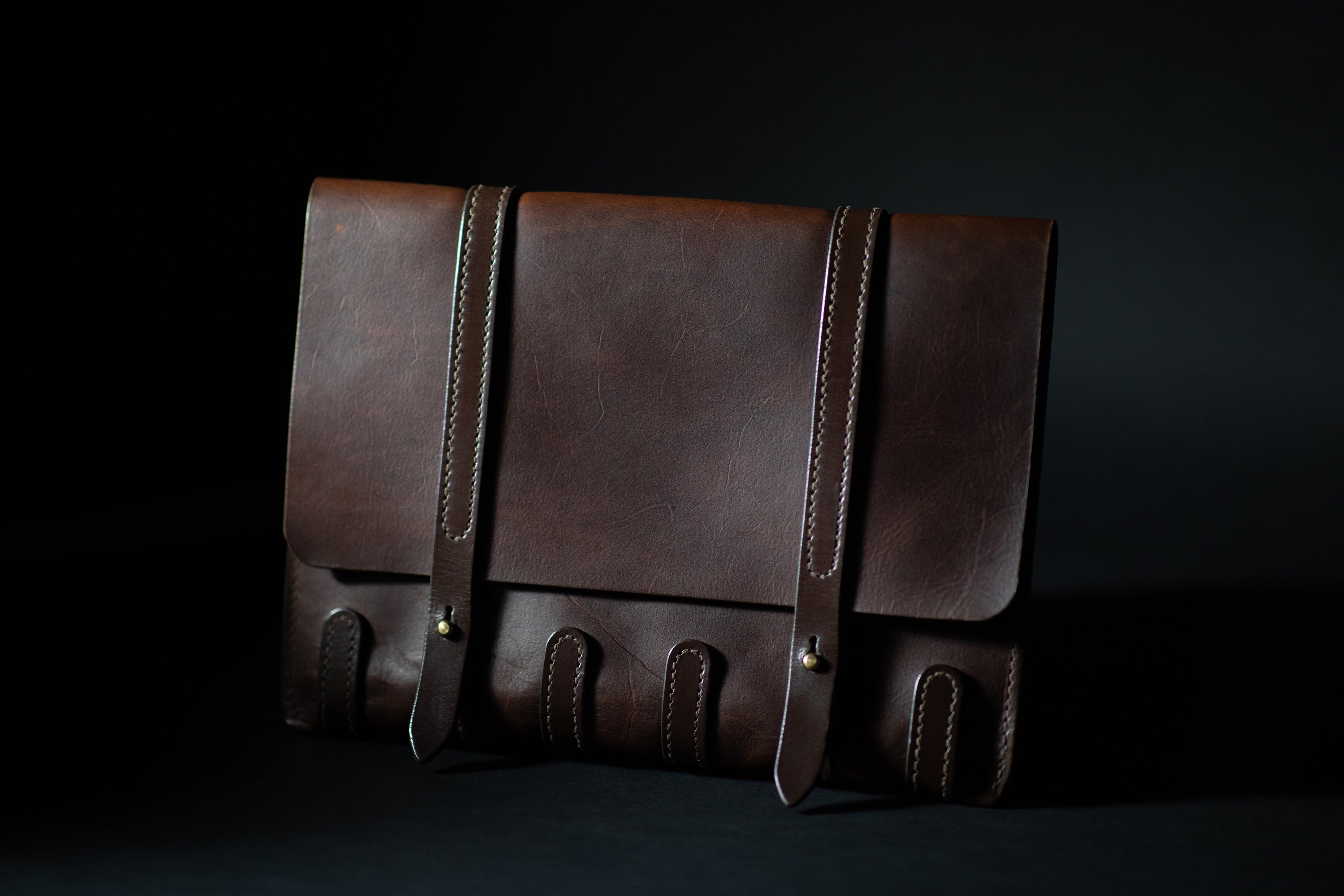 Closed leather folder with two straps, dark background